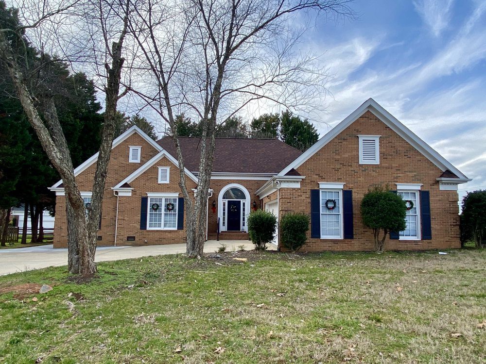 A suburban brick house with gabled roofs and a spacious yard under a clear blue sky.