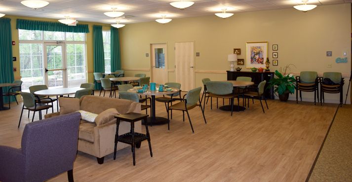 A spacious room featuring a seating area with tables, chairs, and a sofa. A piano is positioned in the corner, enhancing the cozy ambiance.