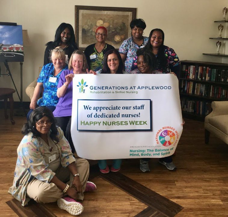 A diverse group of people holding a sign celebrating staff appreciation at an indoor event.