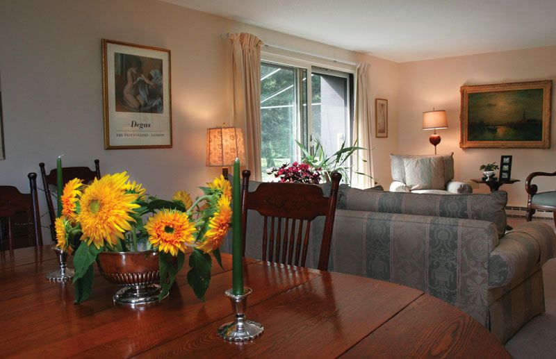 A cozy living and dining area with flowers on the table and comfortable seating by the window.