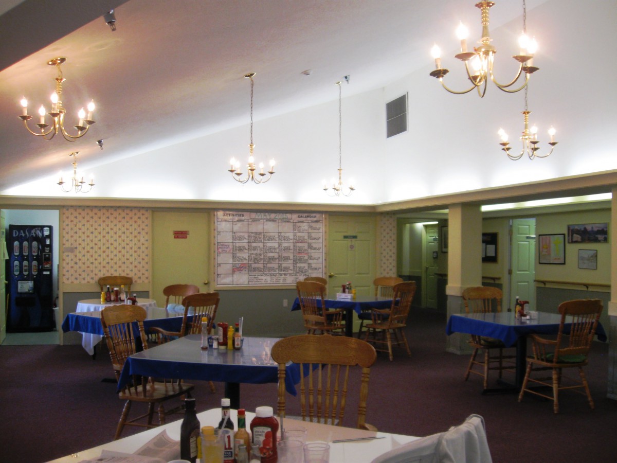 An empty restaurant dining room with wooden chairs and chandeliers.
