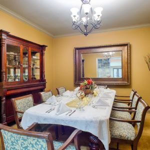 A well-decorated dining room featuring a large table set for a meal, surrounded by chairs and illuminated by a chandelier.