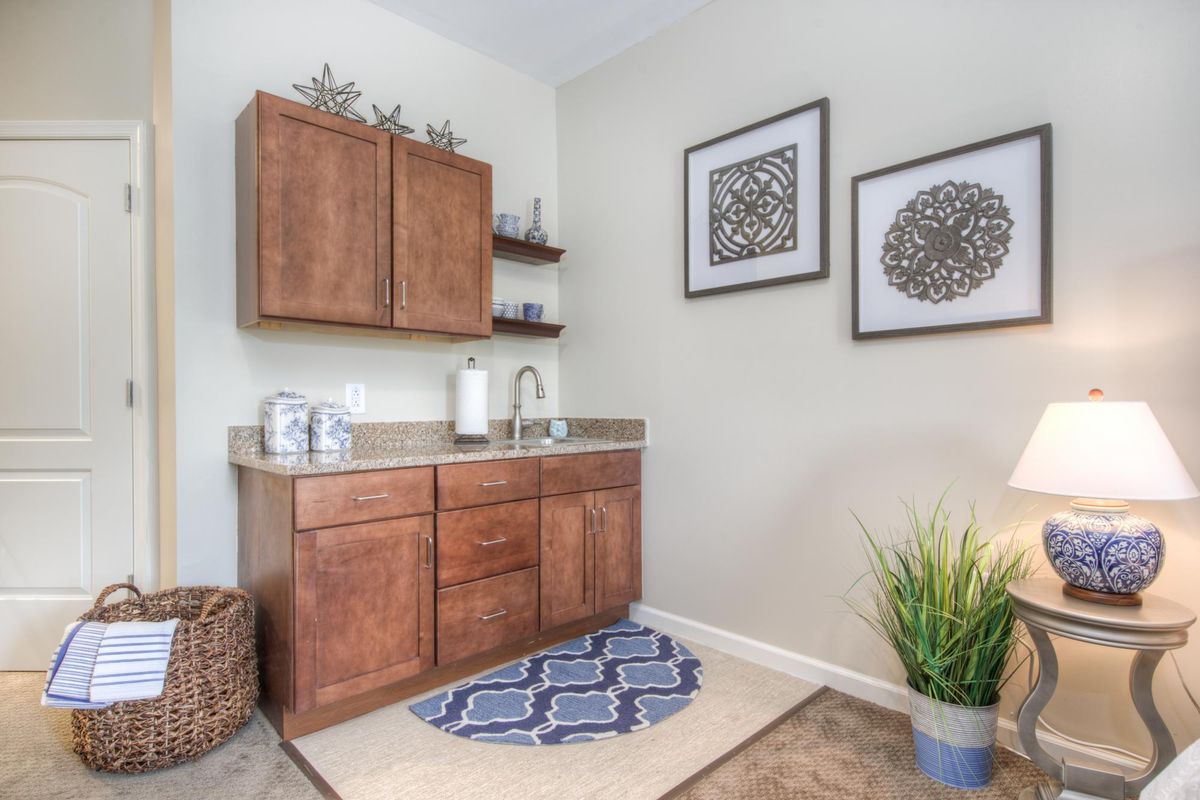 A well-organized laundry room with wooden cabinets, a sink, decorative wall art, and an indoor plant.
