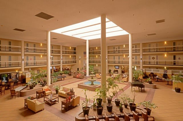 A spacious hotel lobby with abundant seating and greenery under a large skylight.