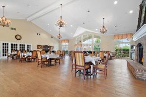 A spacious dining area with elegant chandeliers, neatly arranged tables and chairs, and large windows providing natural light.