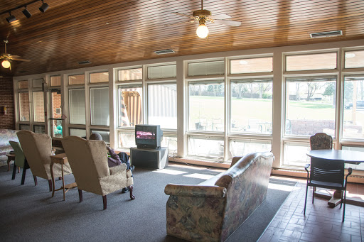A bright and cozy living room featuring a floral sofa, an armchair, and a television, illuminated by natural light.