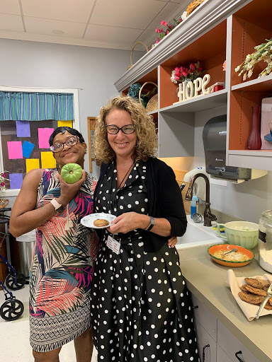 Two women enjoying a moment in the kitchen, one holding an apple and the other a plate of food.