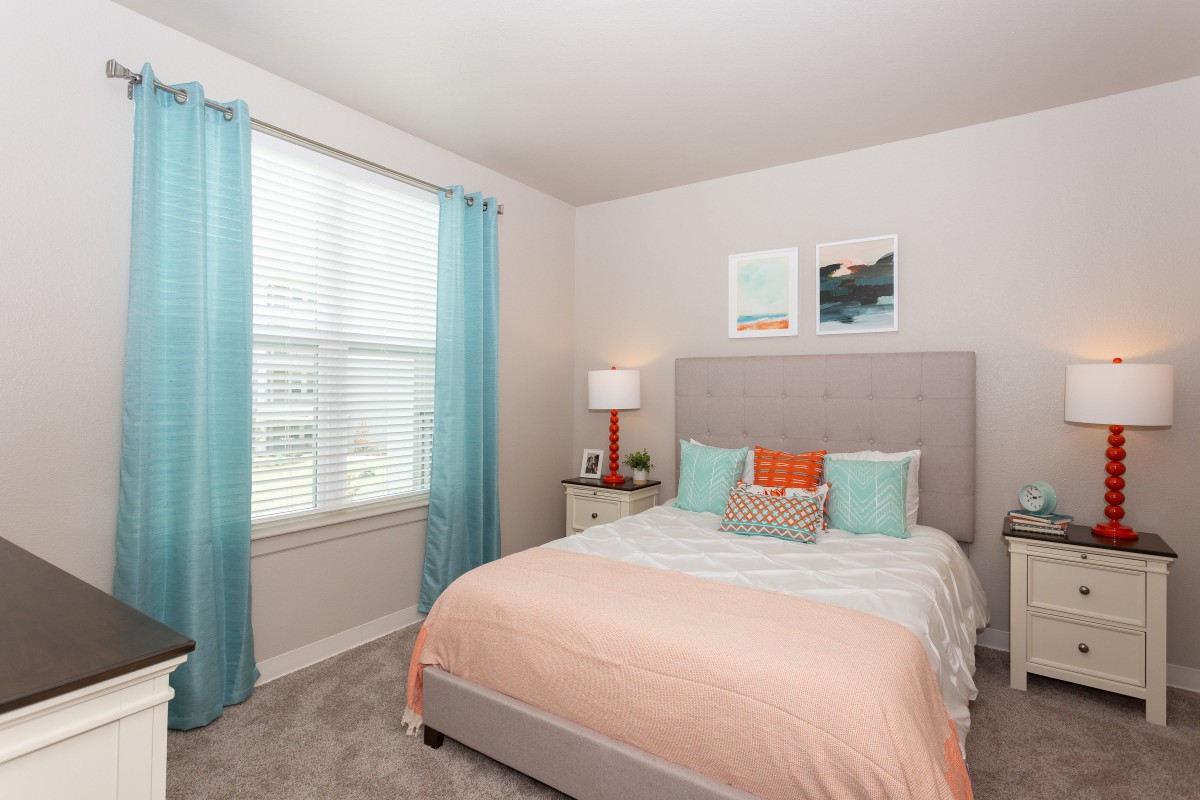 A cozy bedroom with pastel decor and natural light from a large window.