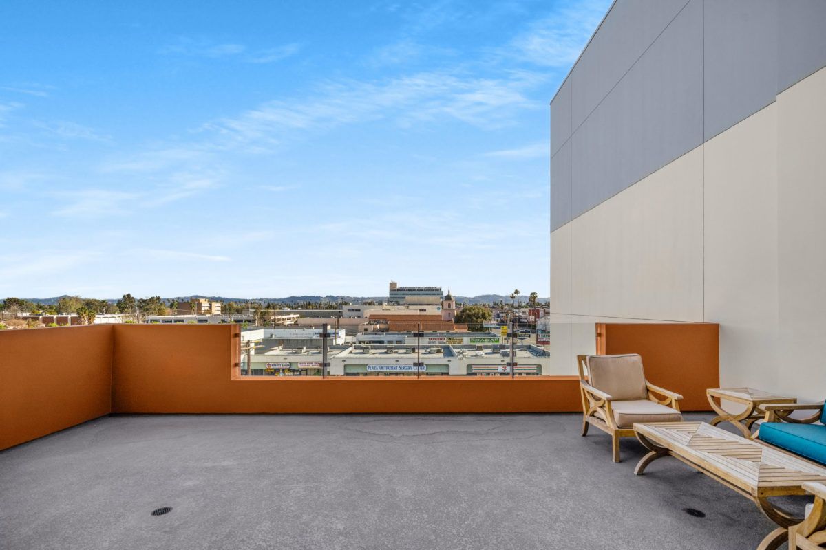 A spacious rooftop terrace with seating offers a panoramic view of the city's skyline against a backdrop of clear blue skies.