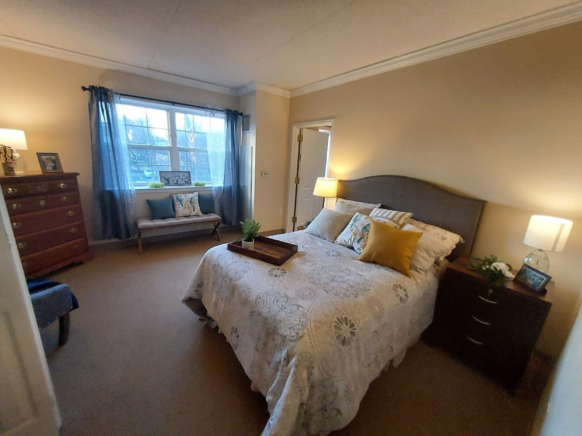 A cozy bedroom with modern decor and neutral tones, featuring a bed with decorative pillows and a large window letting in natural light.
