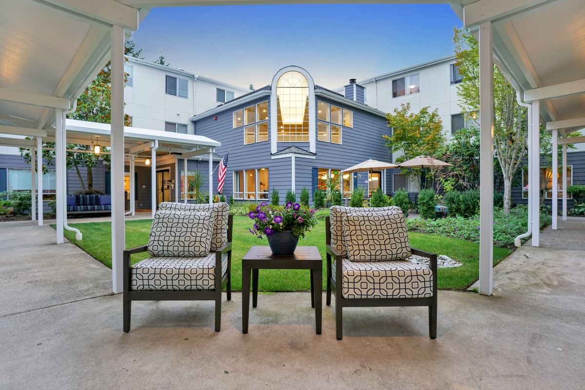 A cozy patio with two chairs and a table overlooking a garden and building.