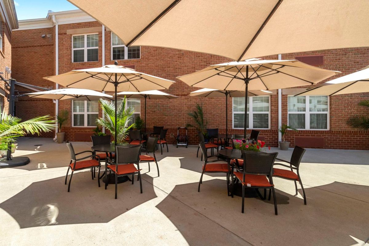 A sunny outdoor patio with tables, chairs, and umbrellas set against a brick building.