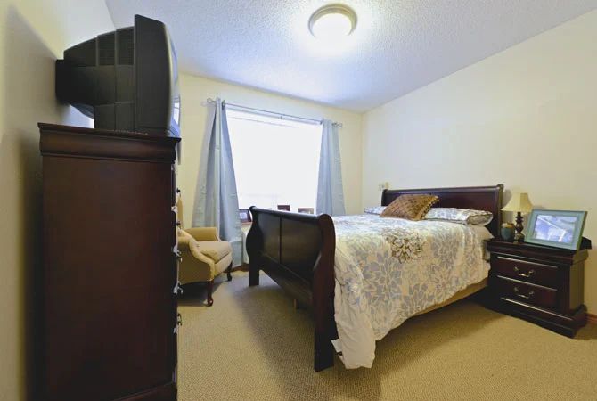 A cozy bedroom featuring a wooden bed, armchair, and television.