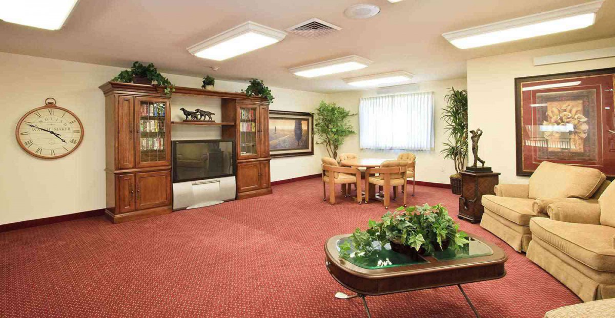 A cozy living room with wooden furniture, a television, indoor plants, and a red carpet.