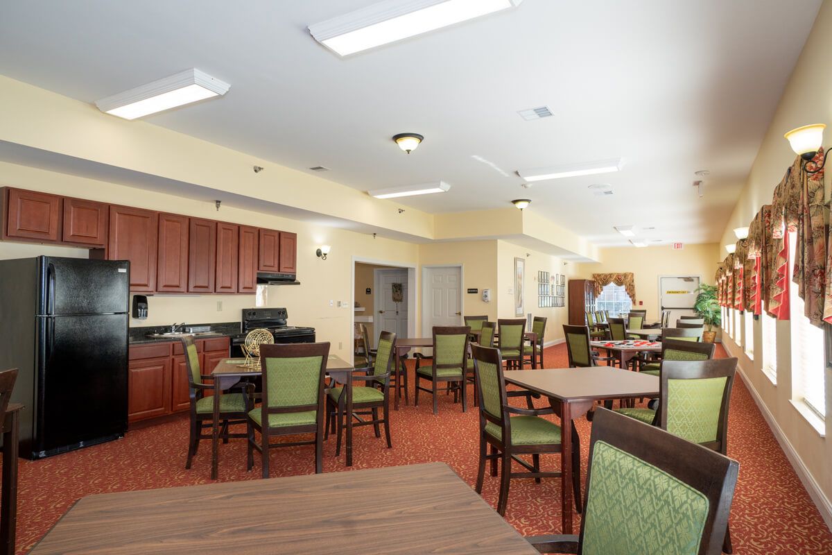A spacious dining area with multiple tables and chairs, featuring a kitchen area in the background.