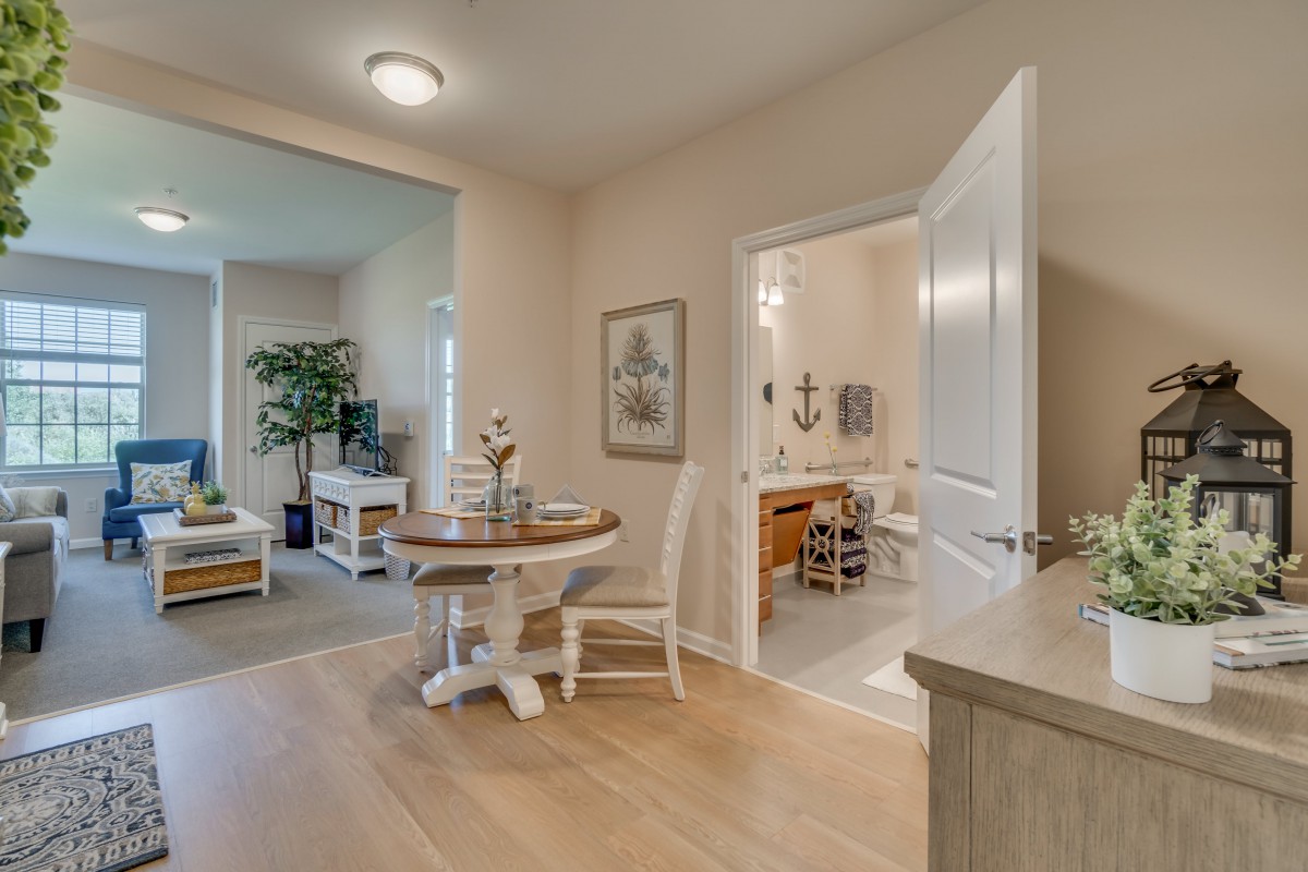 A cozy home interior featuring a dining area with round table and chairs, adjacent to a living room and bathroom.