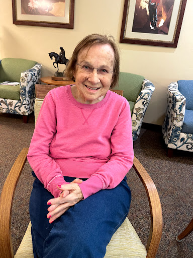 An elderly woman smiles warmly while sitting in a cozy indoor setting.