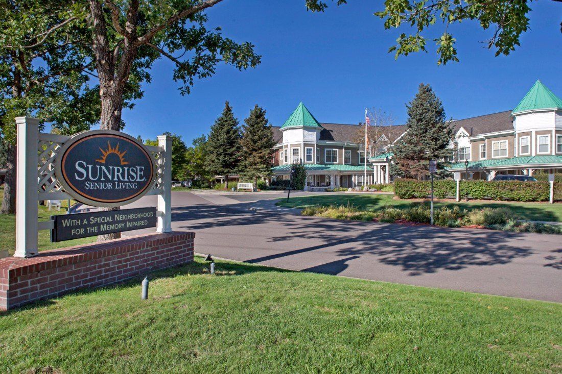 A scenic view of a building with a sign in the foreground, surrounded by trees and grass under a clear blue sky.