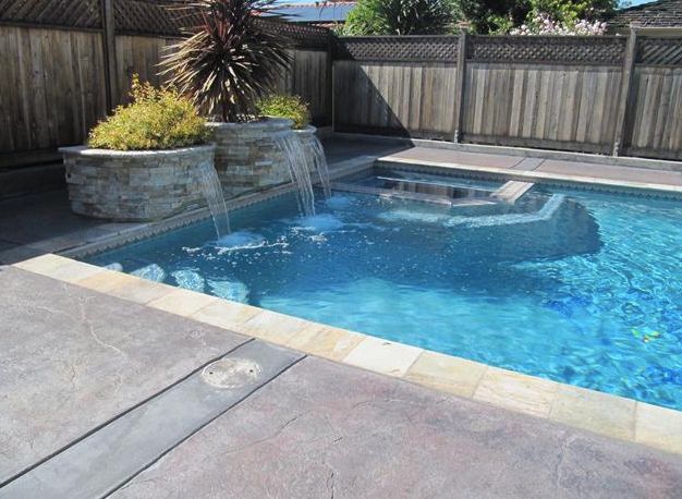 A backyard swimming pool with a small waterfall feature and surrounding patio area.