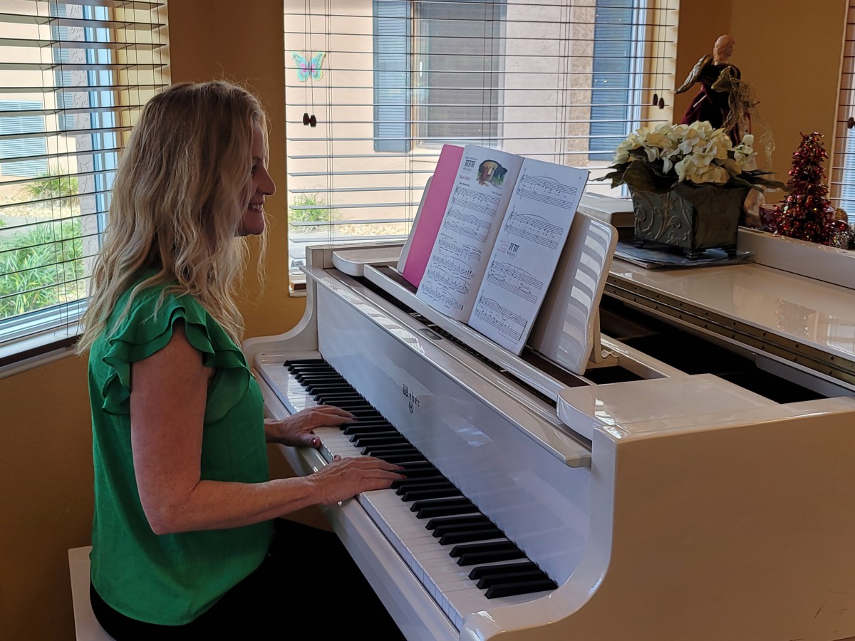 A woman plays the piano while reading sheet music in a well-lit room.