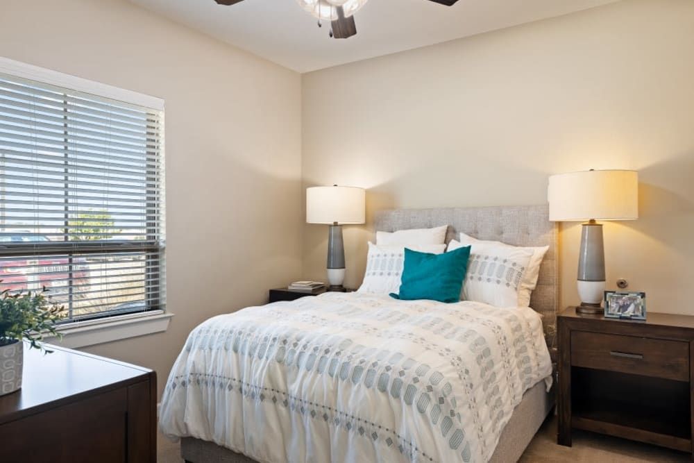 A cozy bedroom featuring a neatly made bed with striped bedding, flanked by two nightstands and lamps, and a window letting in natural light.
