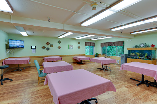 A spacious room with pink tablecloth-covered tables and a warm wooden floor, featuring green walls and ample lighting.