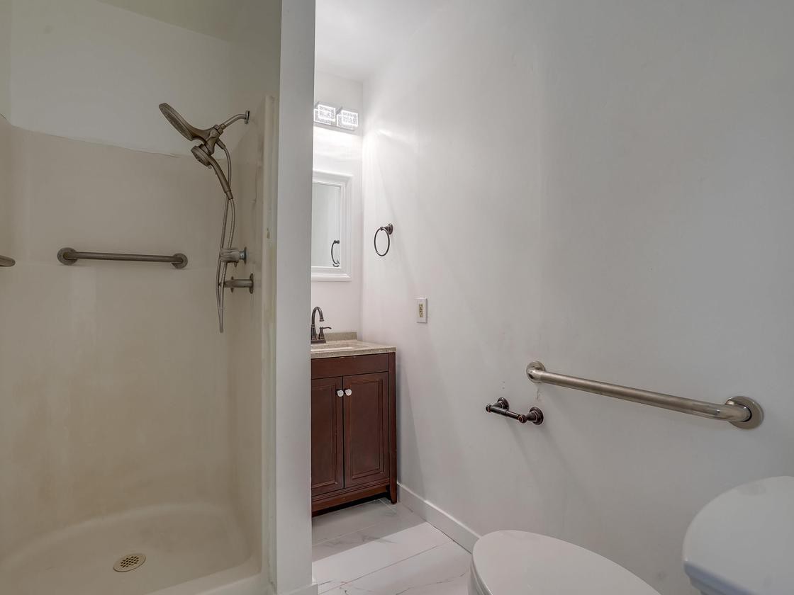 A small bathroom featuring a shower, toilet, and sink with a vanity and mirror.