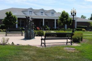 A scenic view of a park with a bench and sculpture in front of a building.