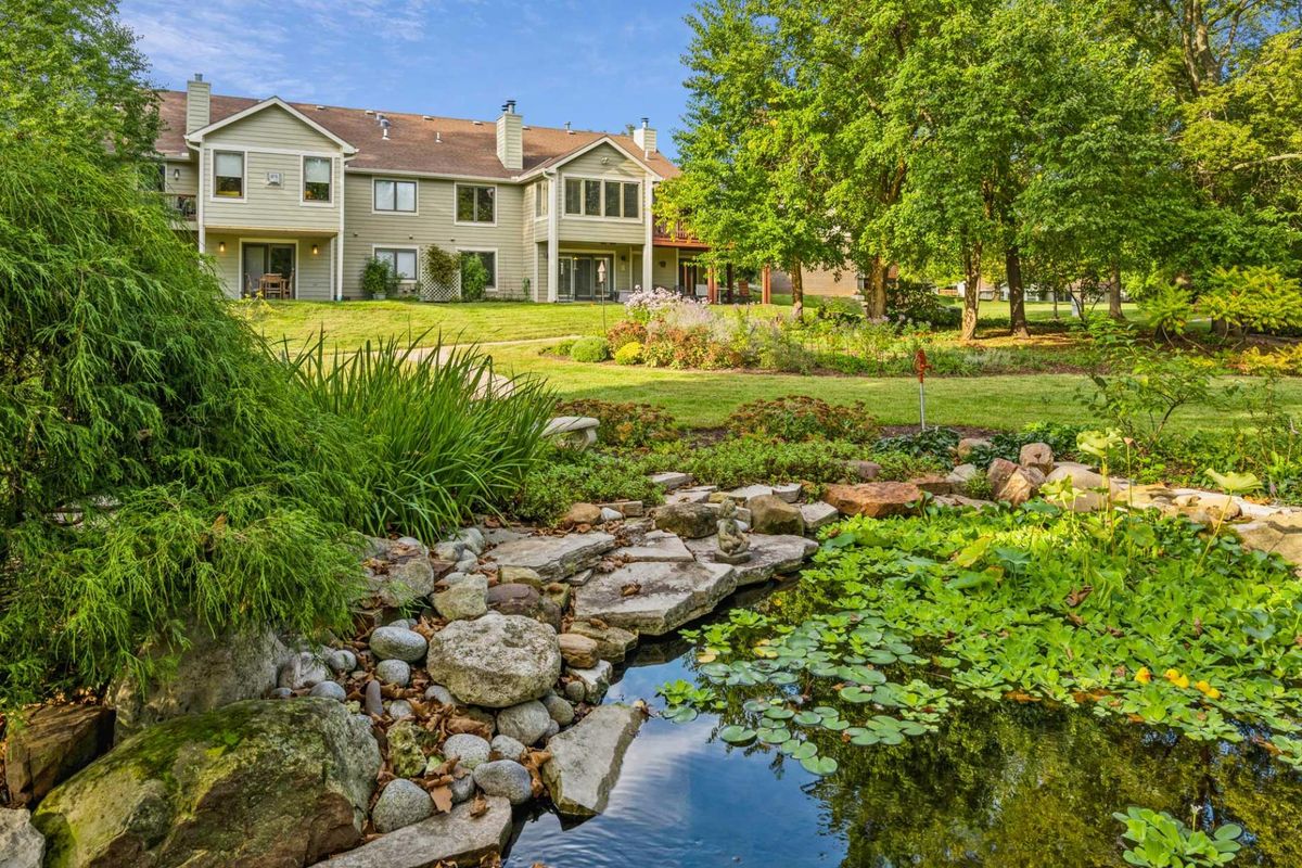A beautiful house surrounded by a lush garden with a pond and trees.