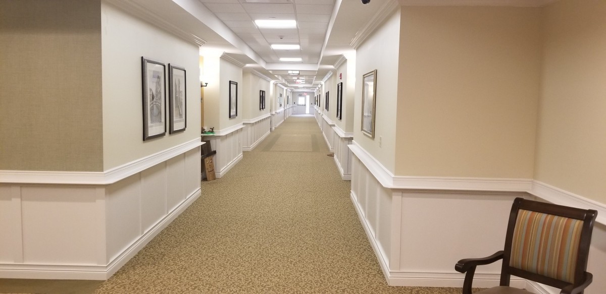 A long hallway with carpeted flooring and framed pictures on the walls.