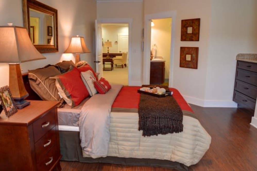 A cozy and well-decorated bedroom with a neatly made bed, featuring warm-toned pillows and a lamp on the bedside table.