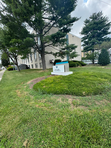 A view of a landscaped area with a sign in front of a building, surrounded by trees and green grass.
