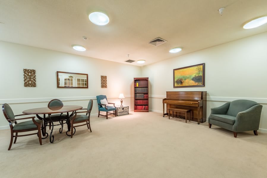 A cozy and well-decorated living room featuring a piano, seating area, bookshelf, and artwork.