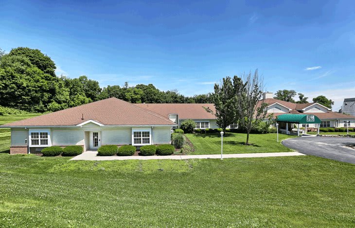 A scenic view of a residential building surrounded by a well-maintained lawn and trees under a clear blue sky.