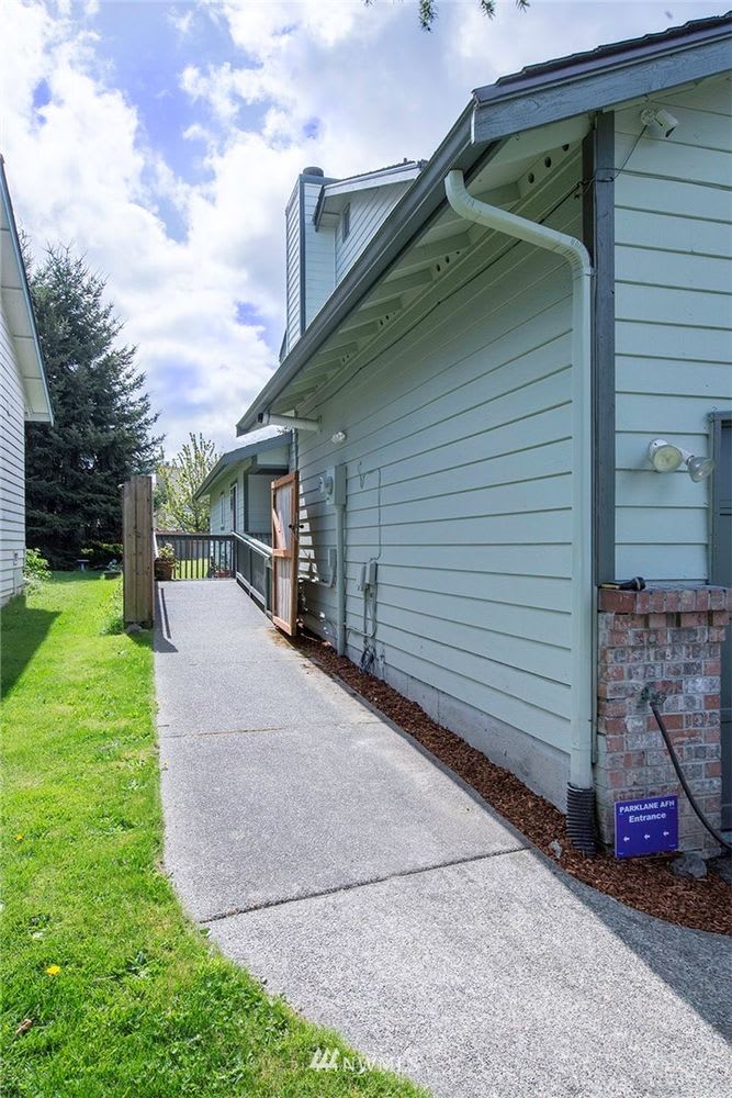 A sunny view of a house exterior with a paved sidewalk and adjacent lawn.