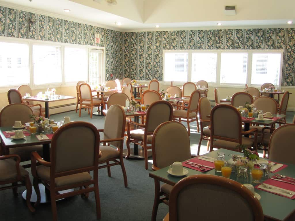 An empty dining room with neatly arranged tables and chairs, featuring large windows and decorative wallpaper.