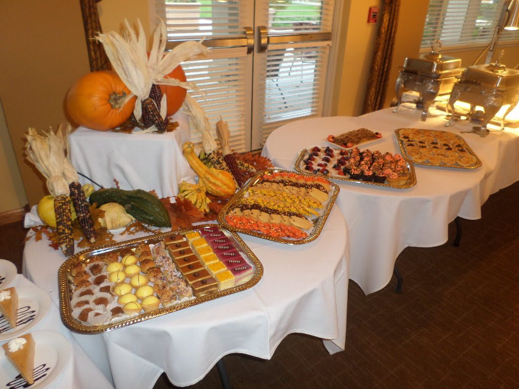 A buffet table elegantly arranged with a variety of desserts and fruits, accented by autumn-themed decorations.