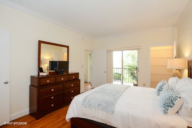 A cozy bedroom with a neatly made bed, dresser and mirror, featuring a sliding door to the balcony.