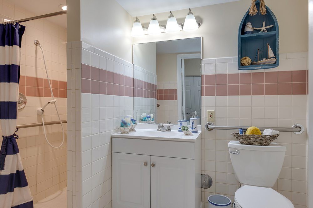A small bathroom featuring a vanity with a mirror, overhead lighting, and tiled walls.