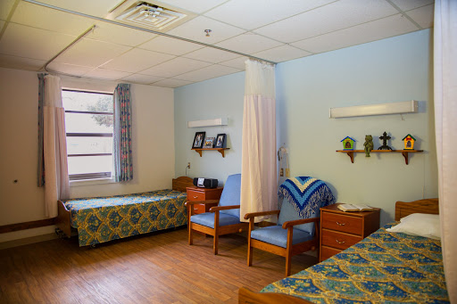 A spacious hospital patient room featuring two beds and a comfortable seating area.