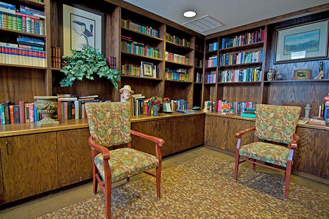 A cozy library corner with bookshelves filled with books and two upholstered chairs.