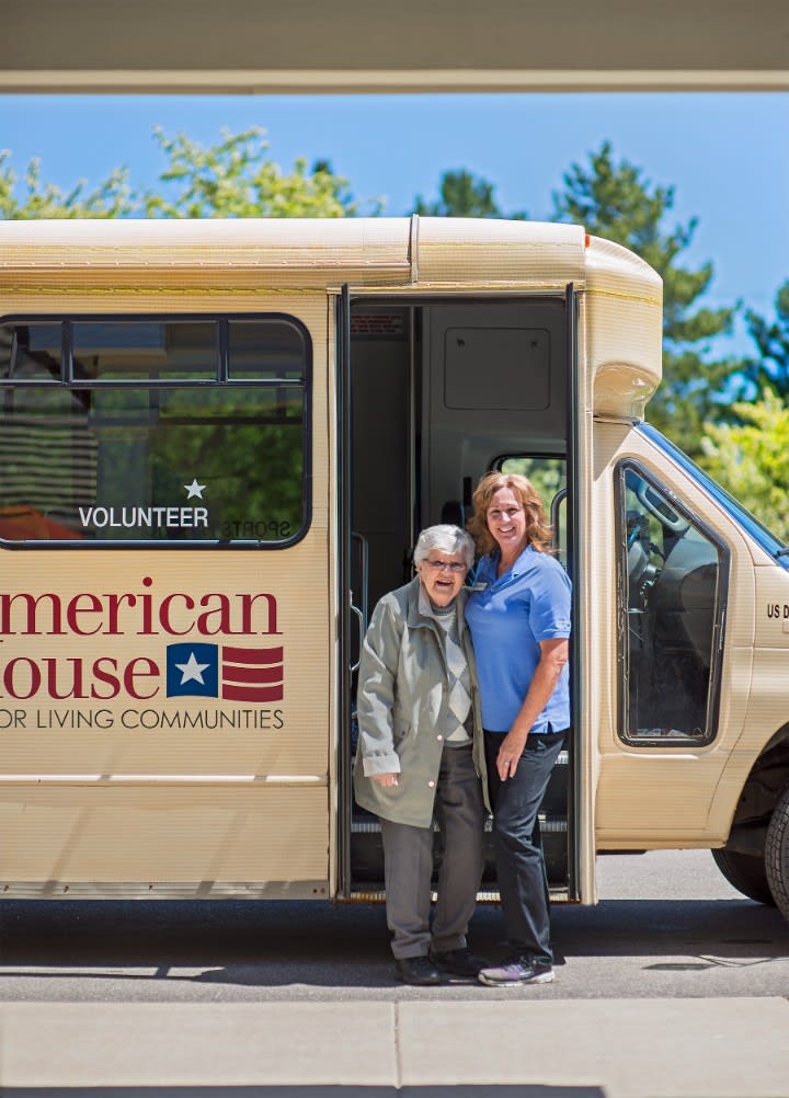 An elderly person and an assistant standing next to a community service bus.