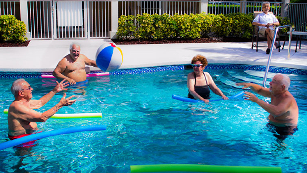 Seniors enjoying a sunny day in the pool with noodles and a beach ball.
