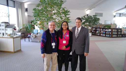 A group of three individuals posing together in a well-lit indoor space, surrounded by greenery.