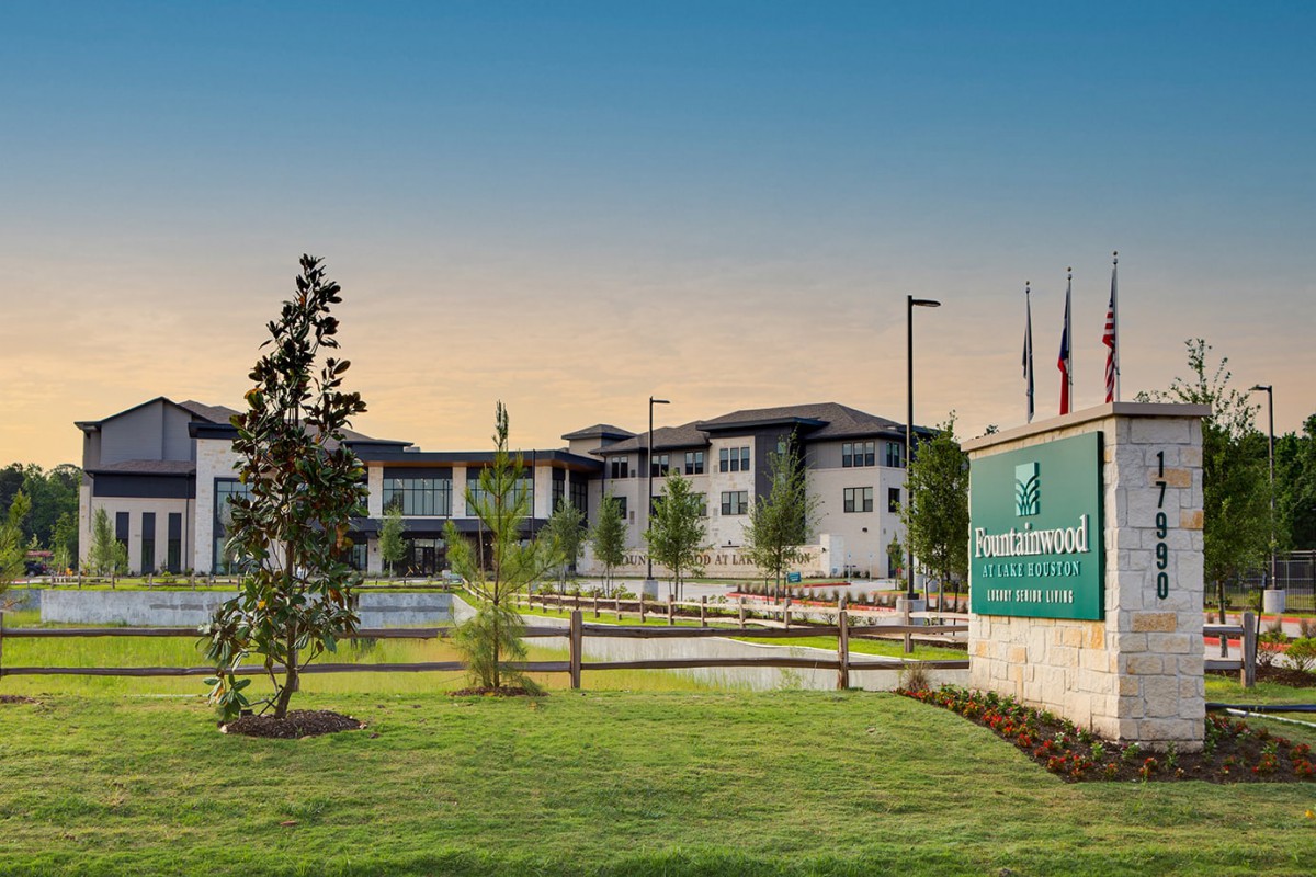A modern building complex with well-maintained lawns and a prominent sign at sunset.