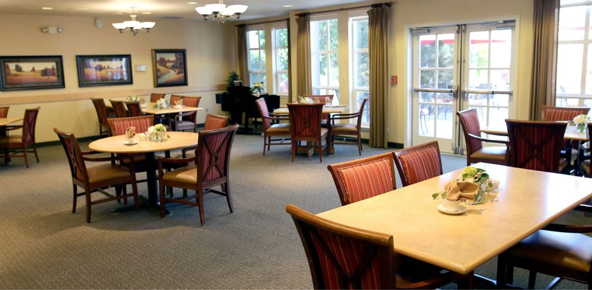 An elegantly arranged dining room with tables and chairs, featuring large windows for natural light.