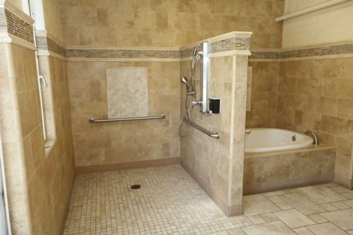 A spacious bathroom with a walk-in shower and bathtub, featuring tiled walls and accessibility grab bars.