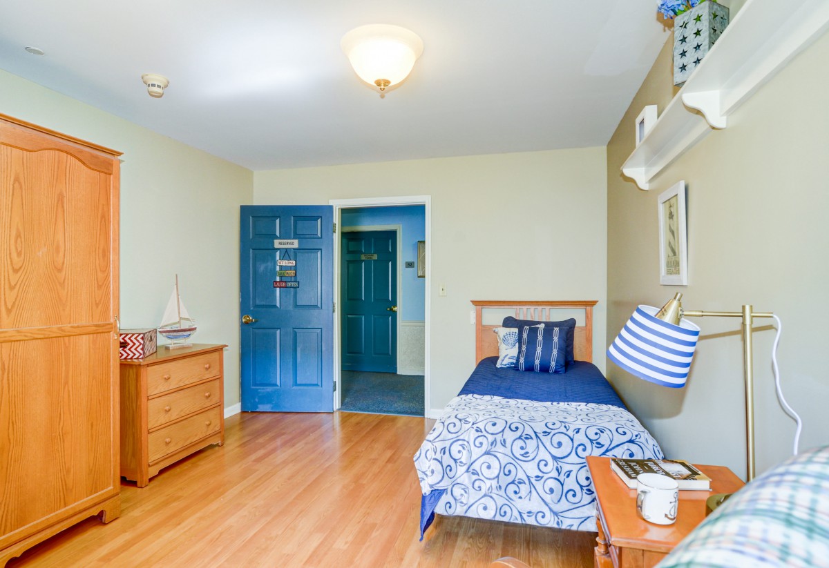A cozy bedroom with a single bed, blue-themed decor, and wooden flooring.