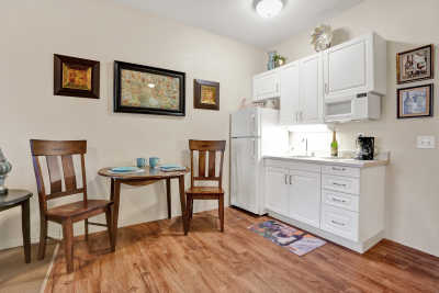 A cozy kitchen and dining area featuring white cabinets, a small table with two chairs, and decorative artwork on the walls.
