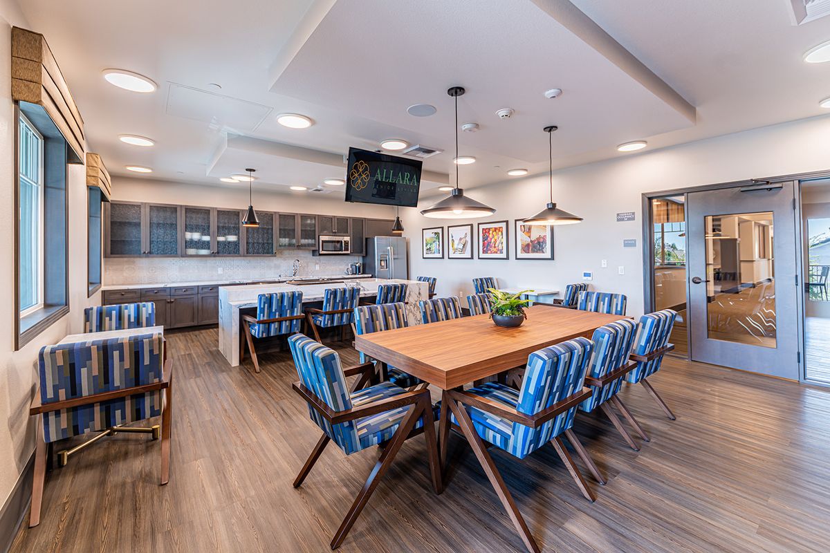 A modern dining area with a large wooden table surrounded by blue chairs, featuring an open kitchen in the background.